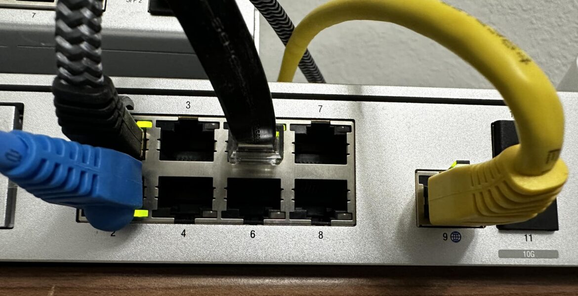 Network switch with blue and yellow Ethernet cables plugged into ports, showing port numbers and cables in use.
