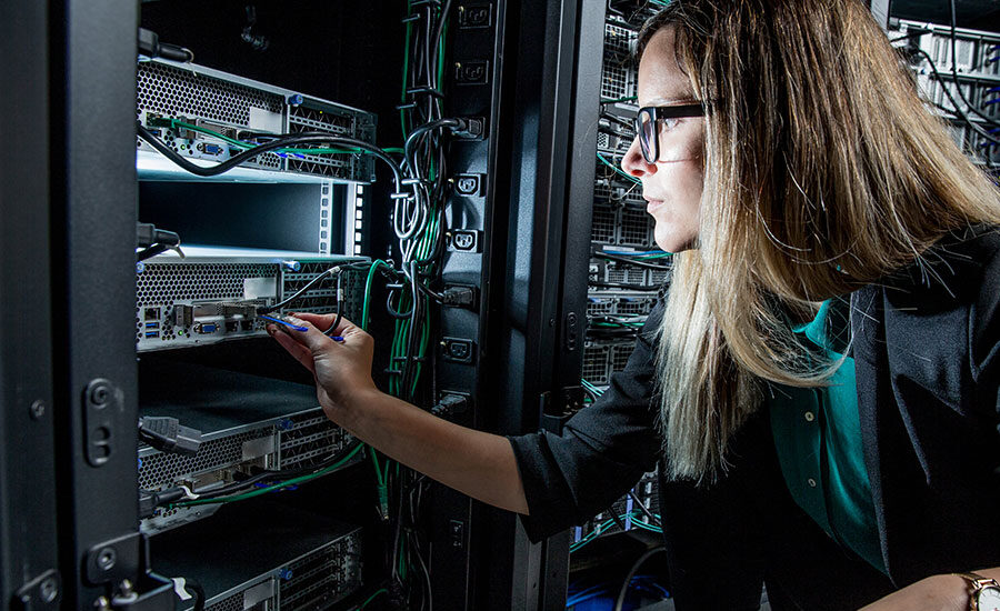 Female IT technician in a data center plugs a network cable into a rack-mounted server.